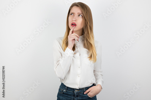 young beatuiful blond woman looks thoughtful standing on isolated white background, body language