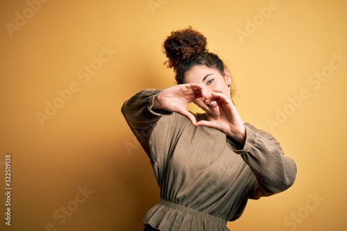 Young beautiful brunette woman with curly hair and piercing wearing casual dress smiling in love doing heart symbol shape with hands. Romantic concept. © Krakenimages.com