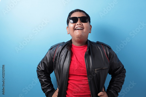 Happy success fat Asian boy wearing leather jacket and sunglasses shows winning gesture