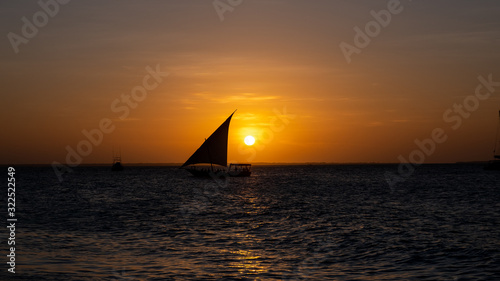 Sunset on a beach in Zanzibar with a boat silhouette in the sun 