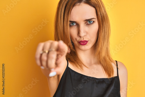 Close up of caucasian elegant woman over isolated yellow background pointing with finger to the camera and to you, hand sign, positive and confident gesture from the front