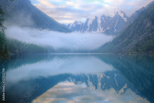 Misty morning on a mountain lake. High mountains with glacier, cold lake and fog. Thick fog swirls over the water.