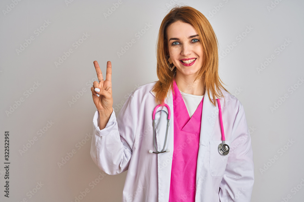 Redhead caucasian doctor woman wearing pink stethoscope over isolated background showing and pointing up with fingers number two while smiling confident and happy. Redhead caucasian doctor woman wearing pink stethoscope over isolated background showing and pointing up with fingers number two while smiling confident and happy.