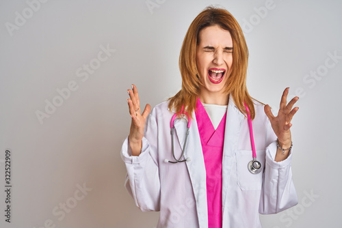 Redhead caucasian doctor woman wearing pink stethoscope over isolated background celebrating mad and crazy for success with arms raised and closed eyes screaming excited. Winner concept