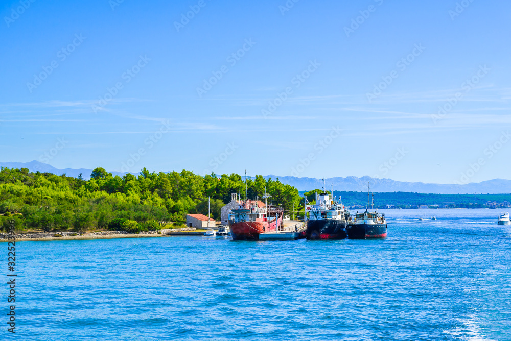 Naklejka premium Cargo ship in the port. Industrial ships on the sea. Transport and logistic concept. Boats in the harbor at the coast of island on Adriatic Sea, Croatia.
