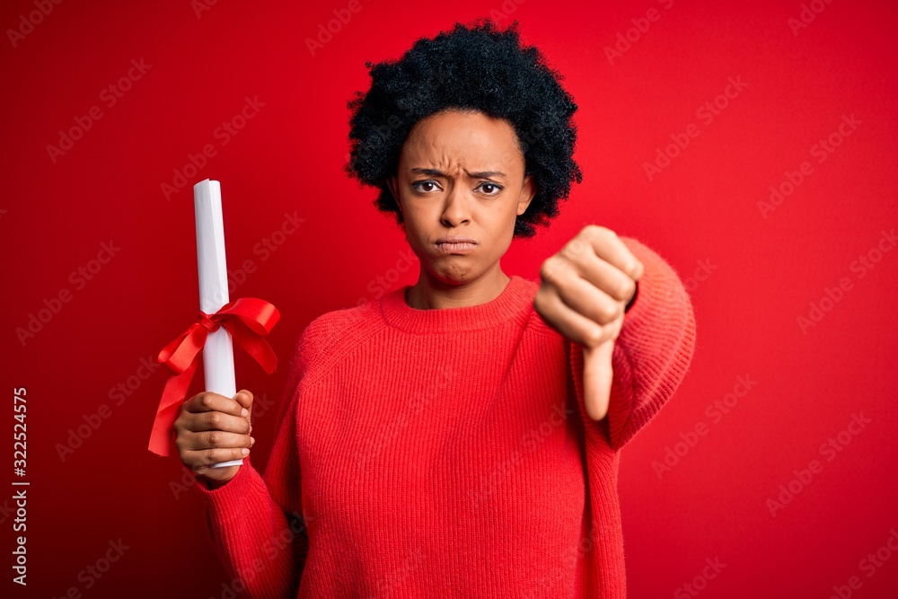 Young African American afro student woman with curly hair holding university degree diploma with angry face, negative sign showing dislike with thumbs down, rejection concept Young African American afro student woman with curly hair holding university degree diploma with angry face, negative sign showing dislike with thumbs down, rejection concept