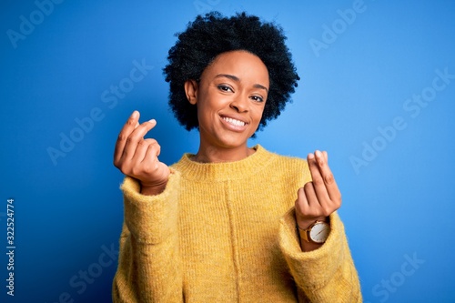 Young beautiful African American afro woman with curly hair wearing yellow casual sweater doing money gesture with hands, asking for salary payment, millionaire business © Krakenimages.com