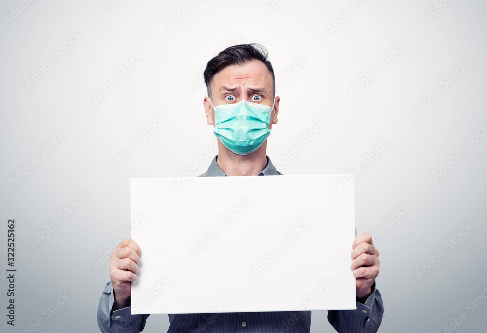 Emotionally frightened young man in a respirator mask holding a white banner. Attention virus concept Emotionally frightened young man in a respirator mask holding a white banner. Attention virus concept