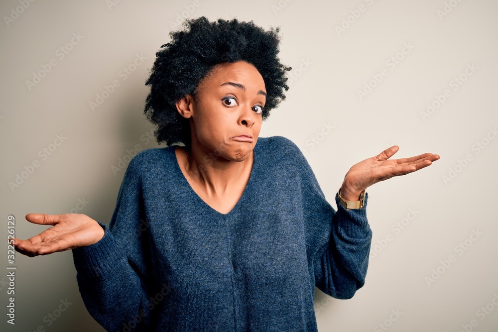 Young beautiful African American afro woman with curly hair wearing casual sweater clueless and confused expression with arms and hands raised. Doubt concept. Young beautiful African American afro woman with curly hair wearing casual sweater clueless and confused expression with arms and hands raised. Doubt concept.