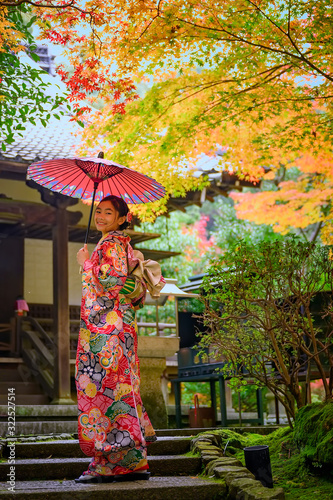 woman holding retro umbrella in old fashion style traditional kimono, stand alone in the middle of park of the village garden in autumn, travel and visit japan on incoming sport event
