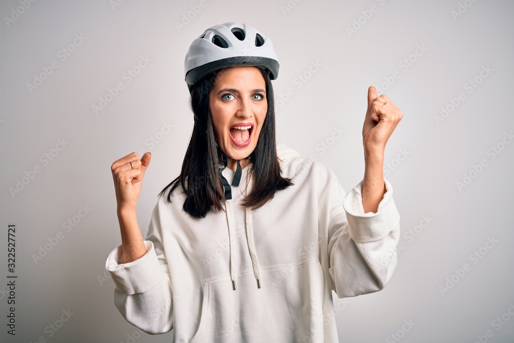 Young cyclist woman with blue eyes wearing bike helmet over isolated white background celebrating surprised and amazed for success with arms raised and open eyes. Winner concept. Young cyclist woman with blue eyes wearing bike helmet over isolated white background celebrating surprised and amazed for success with arms raised and open eyes. Winner concept.