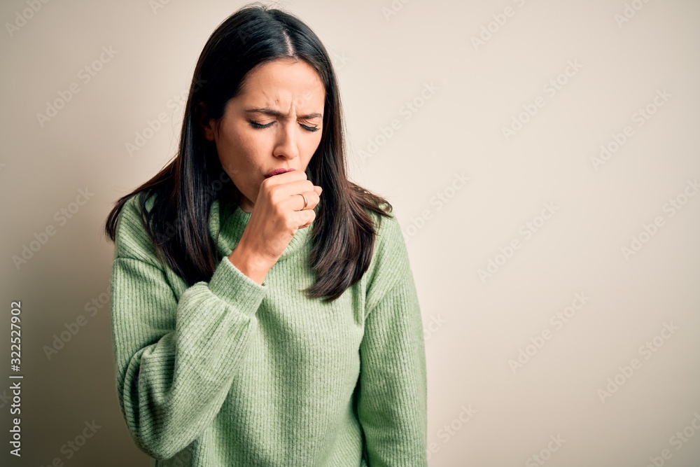 Young brunette woman with blue eyes wearing turtleneck sweater over white background feeling unwell and coughing as symptom for cold or bronchitis. Health care concept. Young brunette woman with blue eyes wearing turtleneck sweater over white background feeling unwell and coughing as symptom for cold or bronchitis. Health care concept.