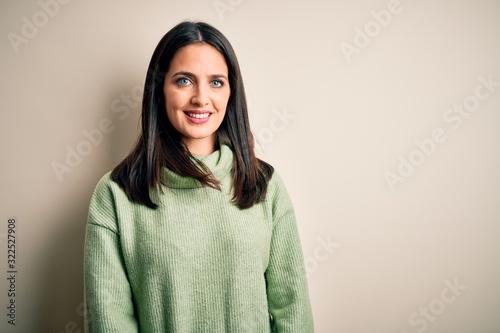 Young brunette woman with blue eyes wearing turtleneck sweater over white background looking away to side with smile on face, natural expression. Laughing confident. © Krakenimages.com