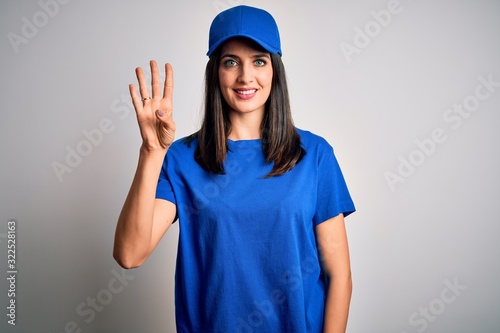 Young delivery woman with blue eyes wearing cap standing over blue background showing and pointing up with fingers number four while smiling confident and happy.