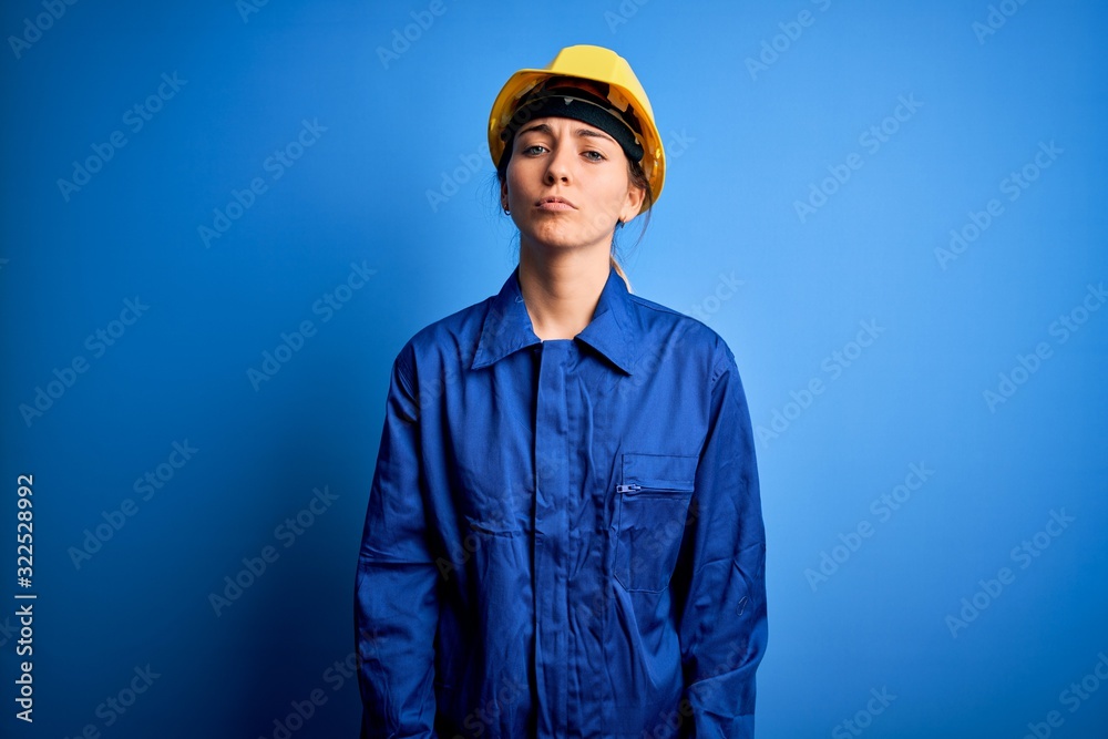 Young beautiful worker woman with blue eyes wearing security helmet and uniform depressed and worry for distress, crying angry and afraid. Sad expression.