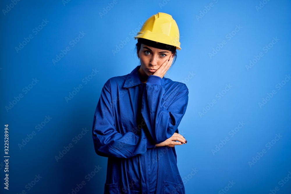 Young beautiful worker woman with blue eyes wearing security helmet and uniform thinking looking tired and bored with depression problems with crossed arms.