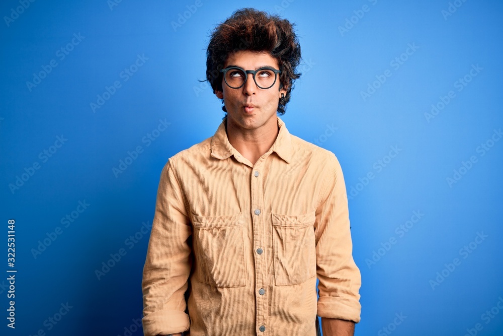 Young handsome man wearing casual shirt standing over isolated blue background making fish face with lips, crazy and comical gesture. Funny expression. Young handsome man wearing casual shirt standing over isolated blue background making fish face with lips, crazy and comical gesture. Funny expression.