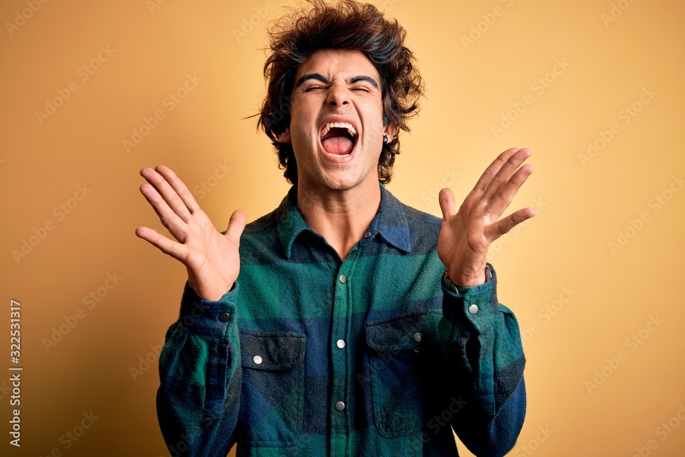 Young handsome man wearing casual shirt standing over isolated yellow background celebrating mad and crazy for success with arms raised and closed eyes screaming excited. Winner concept Young handsome man wearing casual shirt standing over isolated yellow background celebrating mad and crazy for success with arms raised and closed eyes screaming excited. Winner concept