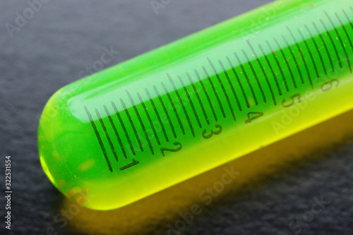 Bright green fluorescent substance in a measuring tube  on a black background. Macro photography.