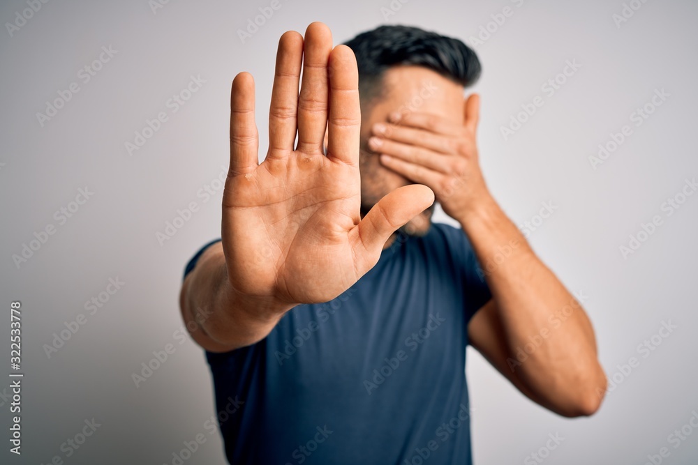 Young handsome man wearing casual t-shirt standing over isolated white background covering eyes with hands and doing stop gesture with sad and fear expression. Embarrassed and negative concept. Young handsome man wearing casual t-shirt standing over isolated white background covering eyes with hands and doing stop gesture with sad and fear expression. Embarrassed and negative concept.