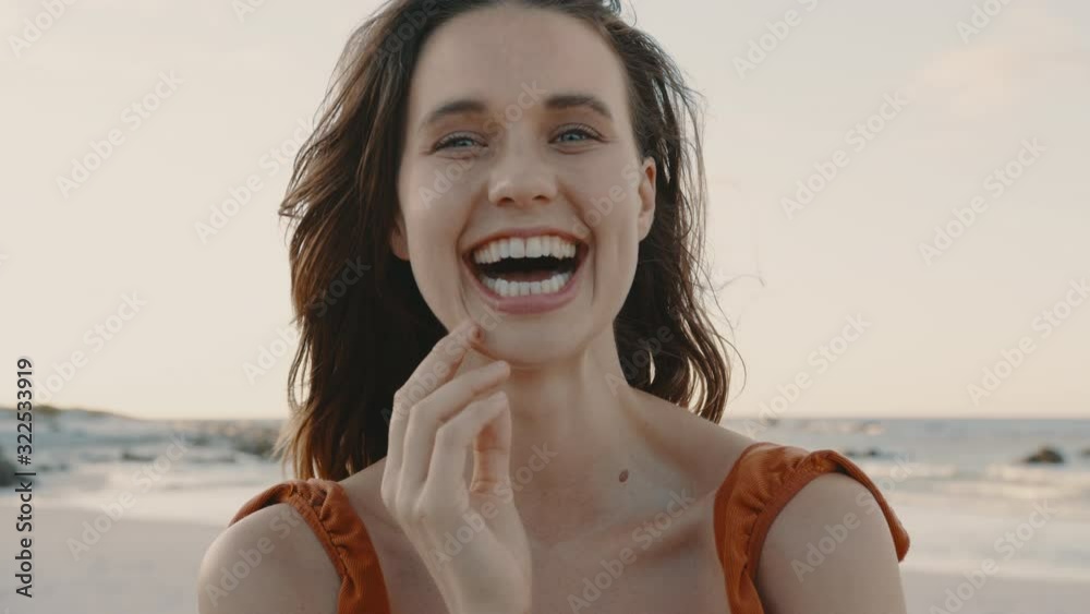 Close up of a pretty woman smiling on the beach. Female model looking at camera and laughing with hand on her face.