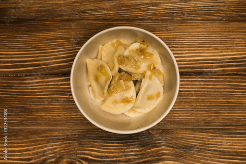 top view of delicious varenyky with fried onion in bowl on wooden table