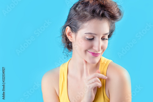 Beautiful brunette girl in a yellow top over a blue background. concept of women's emotions