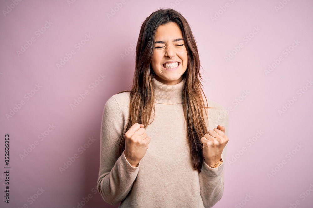 Young beautiful girl wearing casual turtleneck sweater standing over isolated pink background excited for success with arms raised and eyes closed celebrating victory smiling. Winner concept. Young beautiful girl wearing casual turtleneck sweater standing over isolated pink background excited for success with arms raised and eyes closed celebrating victory smiling. Winner concept.
