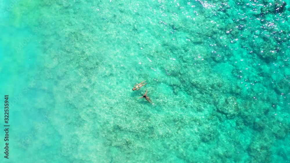 Two girls swim on clear crystal seawater of shallow turquoise lagoon with beautiful rocks and pebbles under water, Seychelles Two girls swim on clear crystal seawater of shallow turquoise lagoon with beautiful rocks and pebbles under water, Seychelles