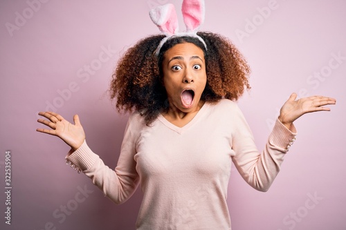 Young african american woman with afro hair wearing bunny ears over pink background celebrating crazy and amazed for success with arms raised and open eyes screaming excited. Winner concept