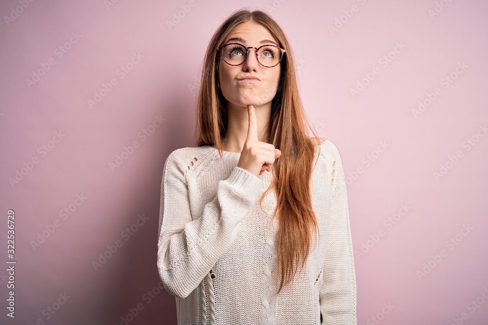 Young beautiful redhead woman wearing casual sweater and glasses over pink background Thinking concentrated about doubt with finger on chin and looking up wondering Young beautiful redhead woman wearing casual sweater and glasses over pink background Thinking concentrated about doubt with finger on chin and looking up wondering