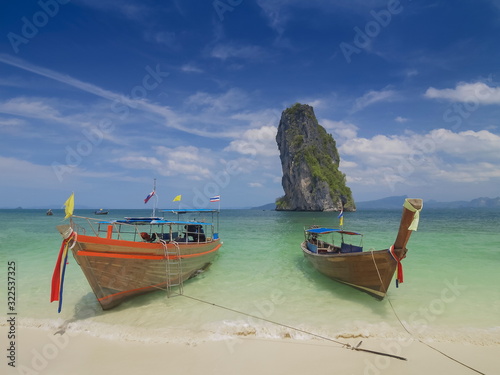 view seaside of two long-tail boats floating in blue-green sea with cliff mountain and cloudy sky background, Ko Poda island, Krabi, southern of Thailand.