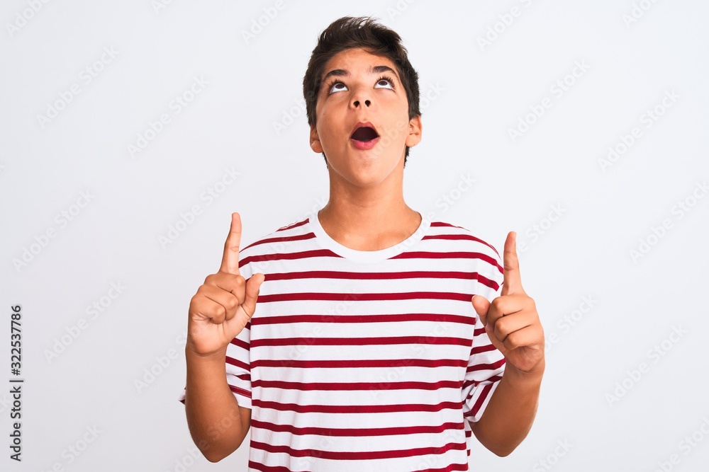 Handsome teenager boy standing over white isolated background amazed and surprised looking up and pointing with fingers and raised arms. Handsome teenager boy standing over white isolated background amazed and surprised looking up and pointing with fingers and raised arms.