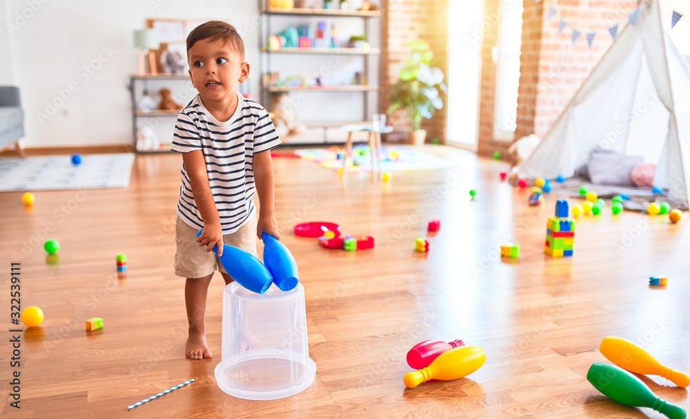 Beautiful toddler boy playing drum using skitlle and plastic basket at kindergarten