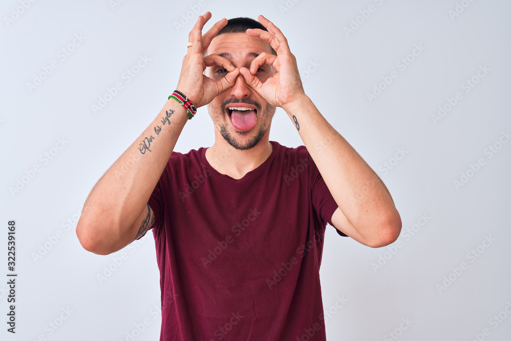 Fototapeta premium Young handsome man standing over isolated background doing ok gesture like binoculars sticking tongue out, eyes looking through fingers. Crazy expression.