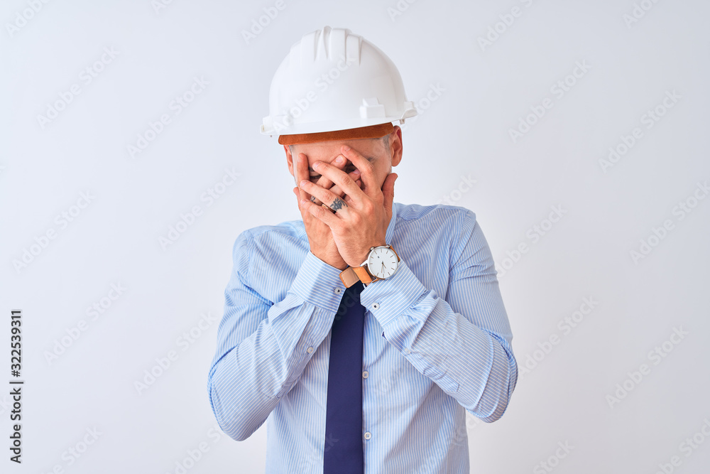 Young business man wearing contractor safety helmet over isolated background with sad expression covering face with hands while crying. Depression concept. Young business man wearing contractor safety helmet over isolated background with sad expression covering face with hands while crying. Depression concept.