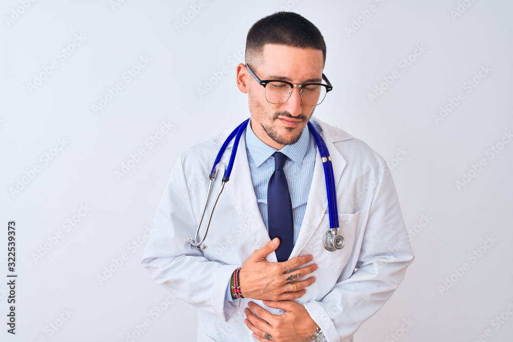 Young doctor man wearing stethoscope over isolated background with hand on stomach because indigestion, painful illness feeling unwell. Ache concept.