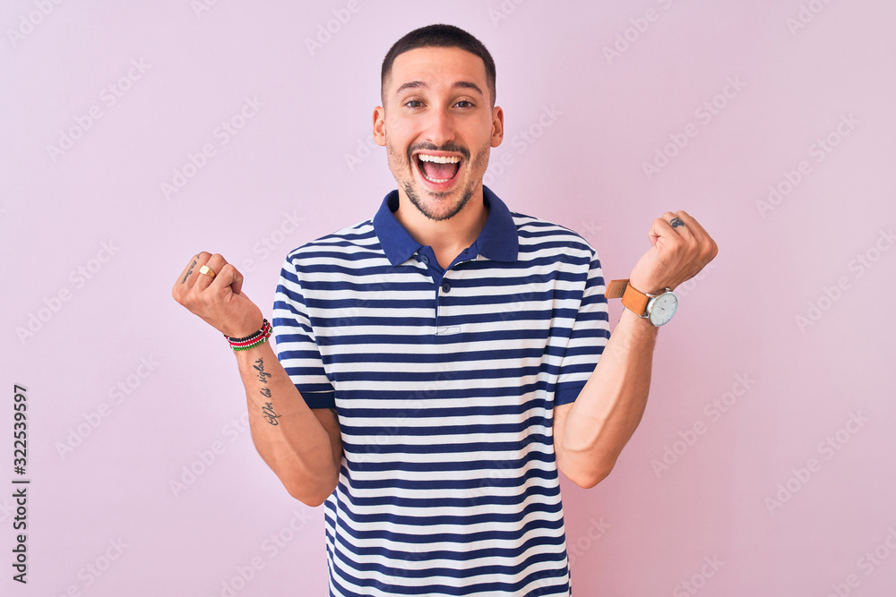 Fototapeta premium Young handsome man wearing nautical striped t-shirt over pink isolated background celebrating surprised and amazed for success with arms raised and open eyes. Winner concept.