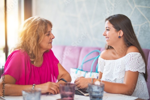 Beautiful mother and daugther sitting at restaurant speaking and smiling