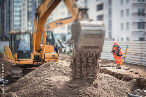 Yellow heavy excavator excavating sand and working during road works, unloading sand during construction of the new road