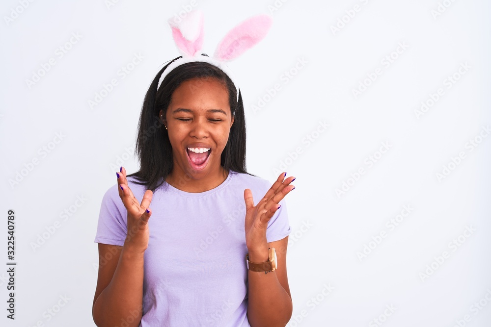 Young african american woman wearing easter rabbit ears over isolated background celebrating mad and crazy for success with arms raised and closed eyes screaming excited. Winner concept Young african american woman wearing easter rabbit ears over isolated background celebrating mad and crazy for success with arms raised and closed eyes screaming excited. Winner concept