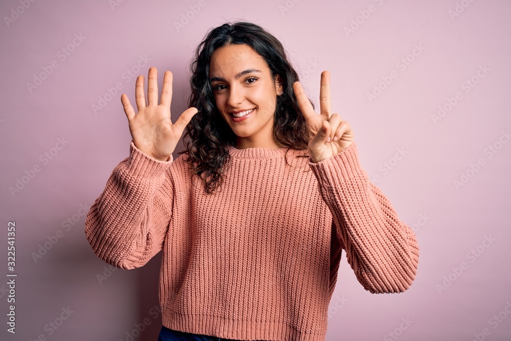 Young beautiful woman with curly hair wearing casual sweater over isolated pink background showing and pointing up with fingers number seven while smiling confident and happy. Young beautiful woman with curly hair wearing casual sweater over isolated pink background showing and pointing up with fingers number seven while smiling confident and happy.
