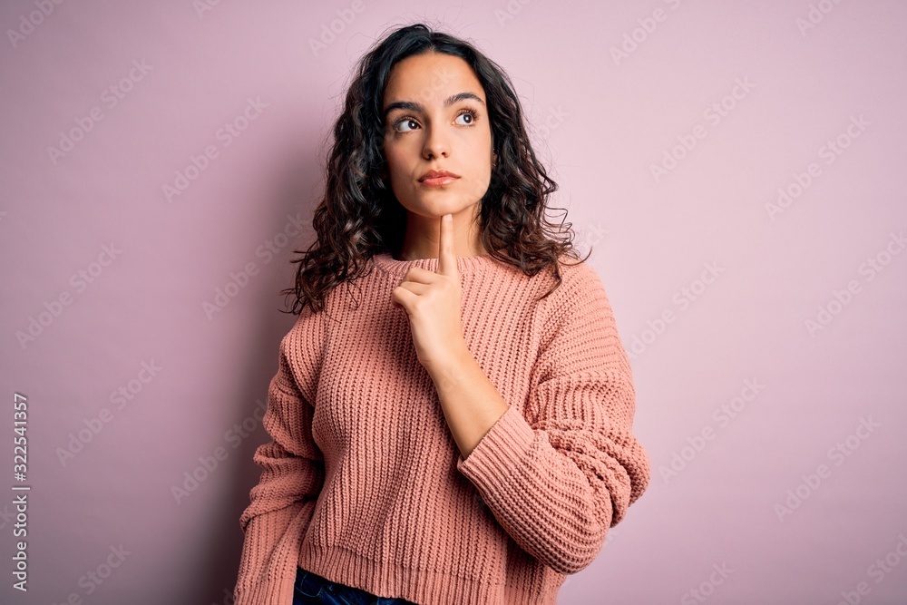 Young beautiful woman with curly hair wearing casual sweater over isolated pink background Thinking concentrated about doubt with finger on chin and looking up wondering Young beautiful woman with curly hair wearing casual sweater over isolated pink background Thinking concentrated about doubt with finger on chin and looking up wondering