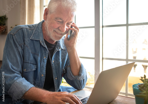 Obraz na plátne Close up of a senior adult man  with beard and white hair working at home using the laptop
