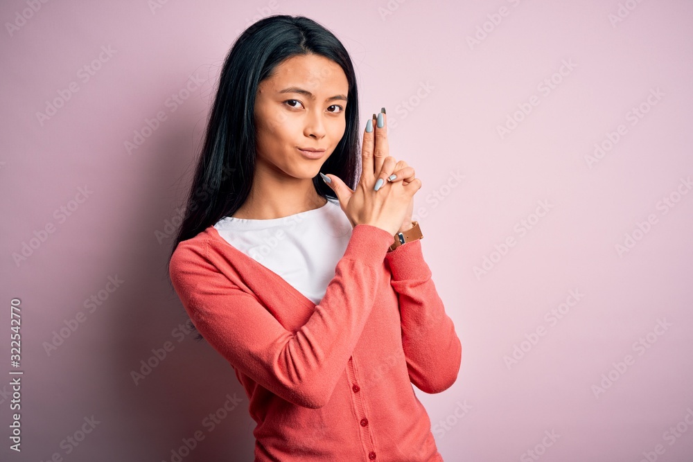 Young beautiful chinese woman wearing casual sweater over isolated pink background Holding symbolic gun with hand gesture, playing killing shooting weapons, angry face Young beautiful chinese woman wearing casual sweater over isolated pink background Holding symbolic gun with hand gesture, playing killing shooting weapons, angry face