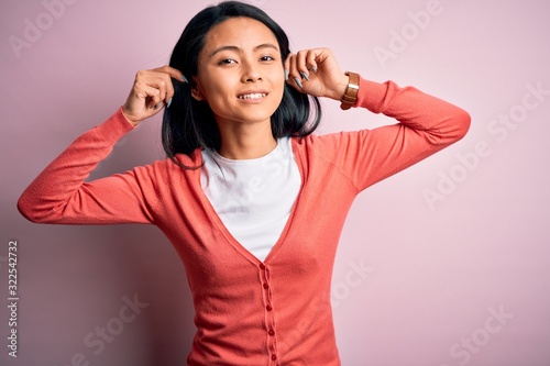 Young beautiful chinese woman wearing casual sweater over isolated pink background Smiling pulling ears with fingers, funny gesture. Audition problem © Krakenimages.com