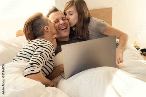 Happy relaxed family of using laptop in bed at home. Mom, father and daughter spending time together in the morning