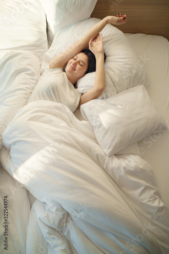 Young woman waking up and streching on bed in the morning. A girl awakes in the morning