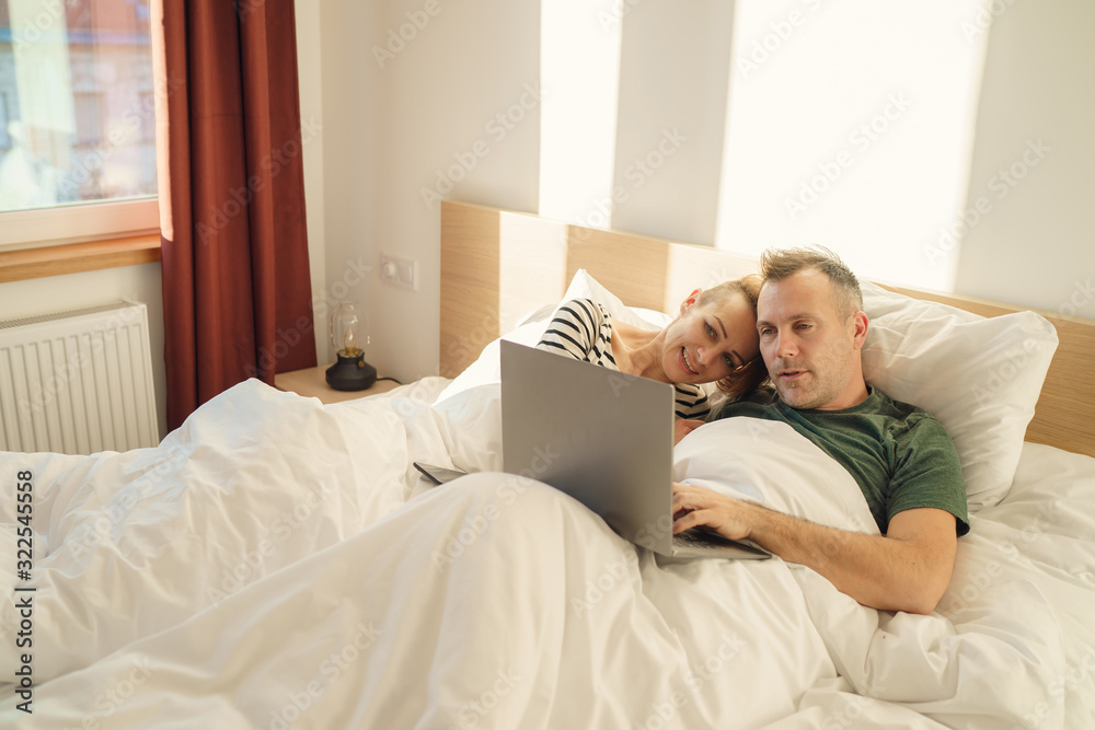 Cheerful couple using a computer lying on their bed at home Cheerful couple using a computer lying on their bed at home