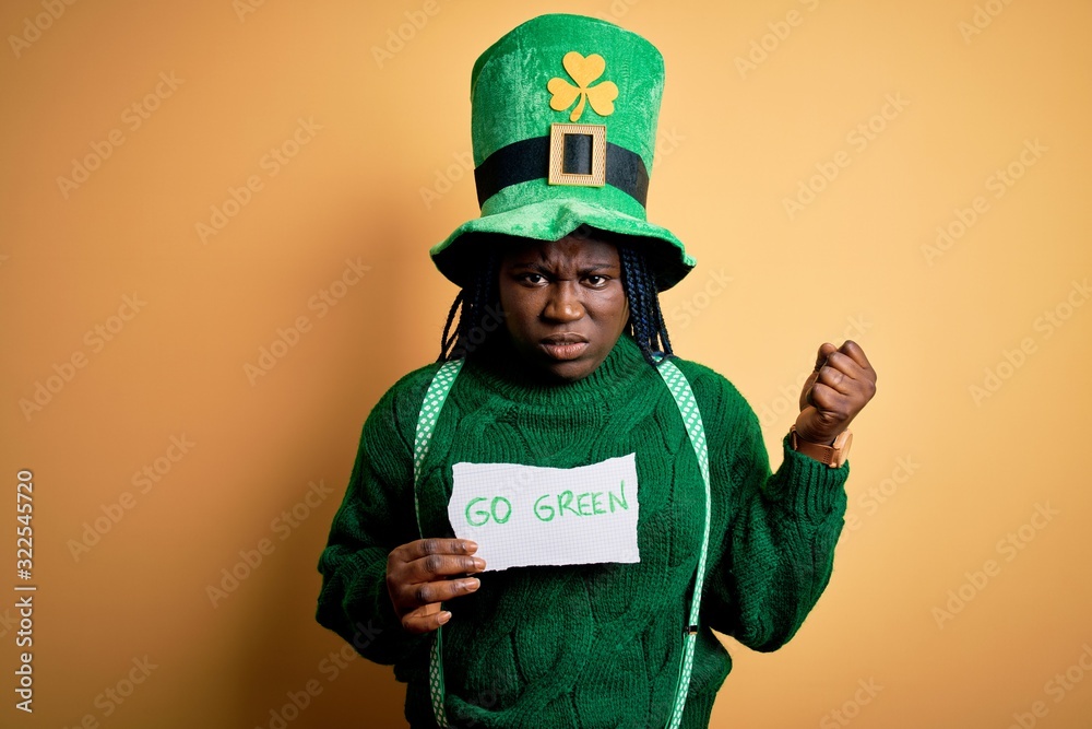 Plus size african american woman wearing green hat holding paper on saint patricks day annoyed and frustrated shouting with anger, crazy and yelling with raised hand, anger concept Plus size african american woman wearing green hat holding paper on saint patricks day annoyed and frustrated shouting with anger, crazy and yelling with raised hand, anger concept